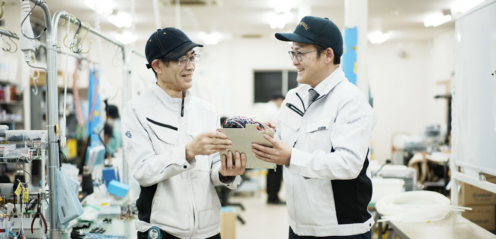 写真：工場内で笑顔で打ち合わせする二人の男性スタッフ